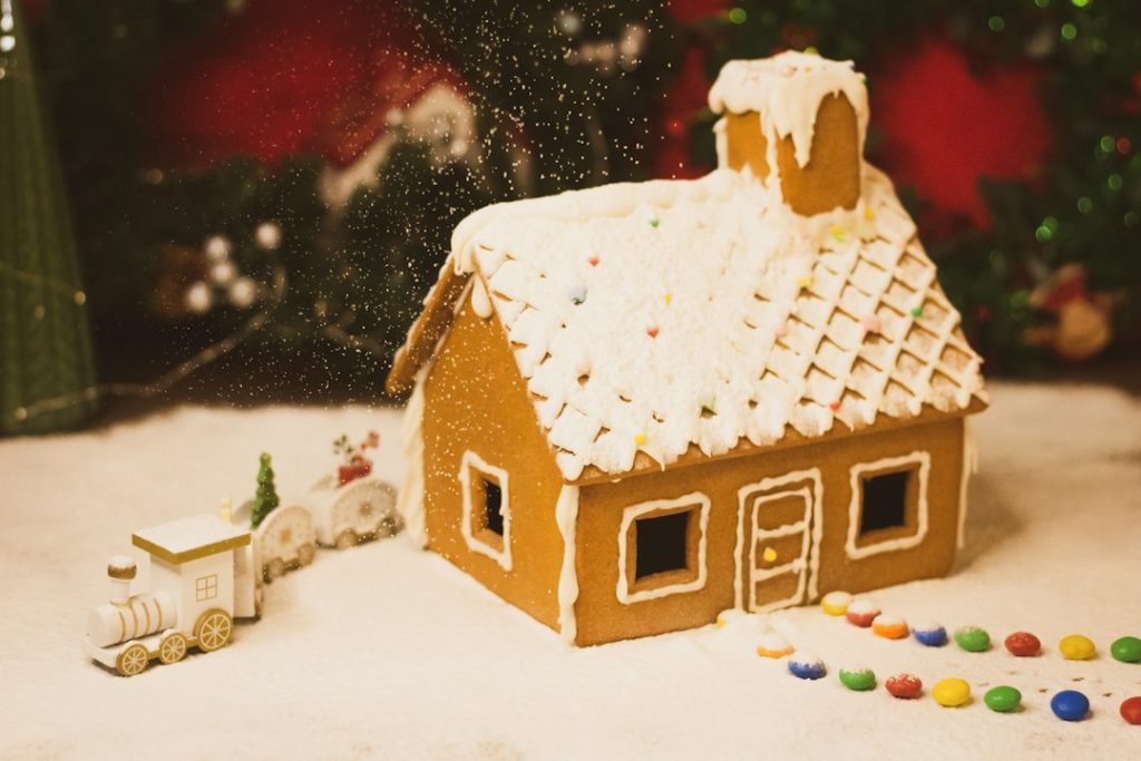 A gingerbread house decorated for the holiday season with a small train and Christmas tree