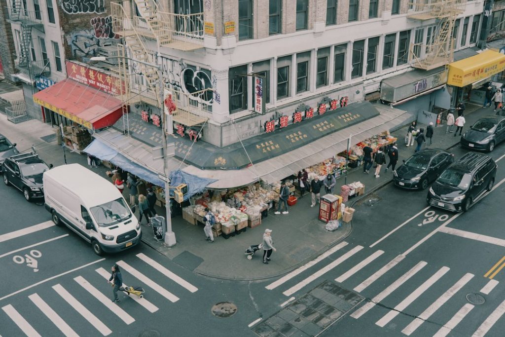 A busy New York neighborhood street with shops and people moving through the area