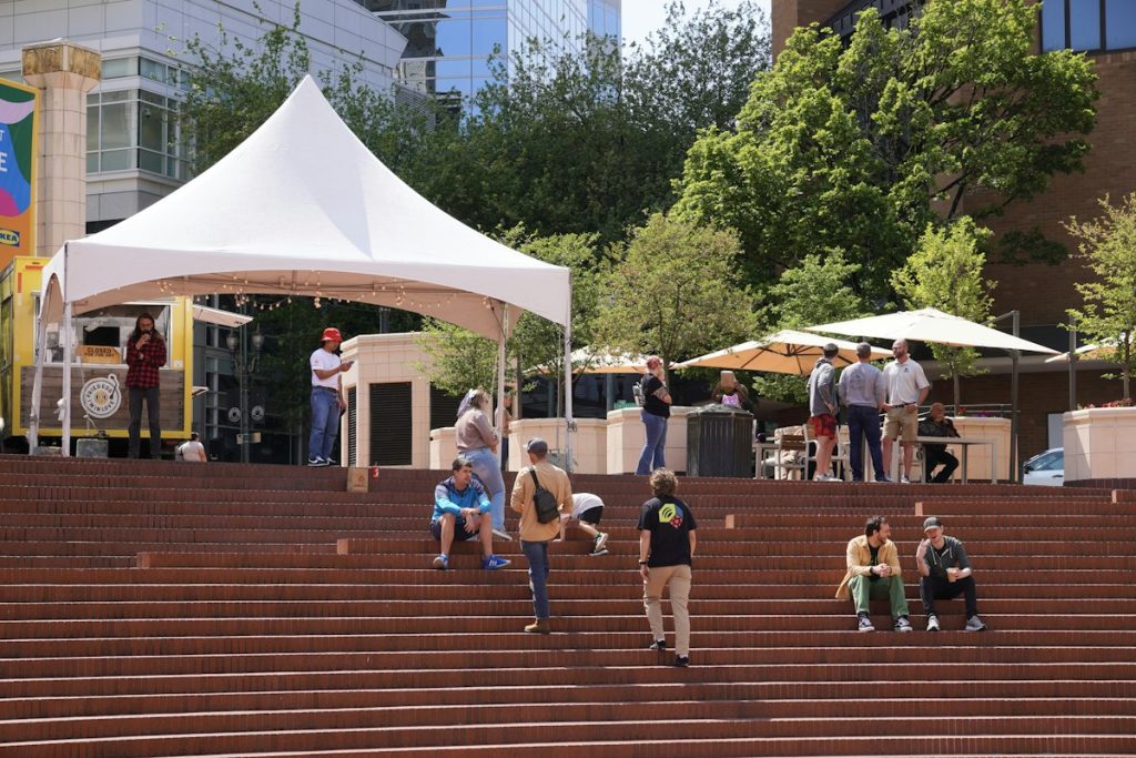 People gathered in a public plaza near a tent and community gathering space